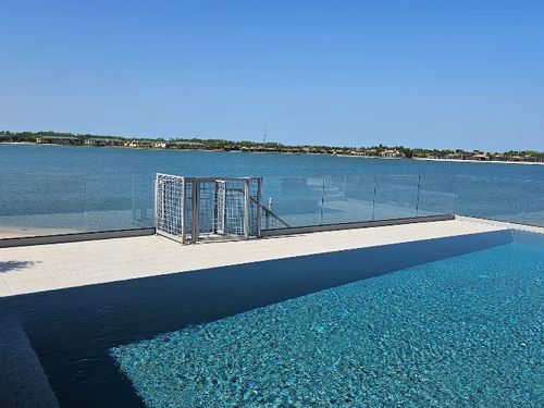 A pool with a glass fence and a bay view behind it