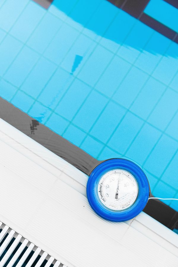 A pool thermometer floating at the tiled edge of a clear pool