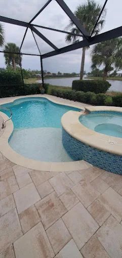 A pool and attached spa on a travertine deck in Fort Myers