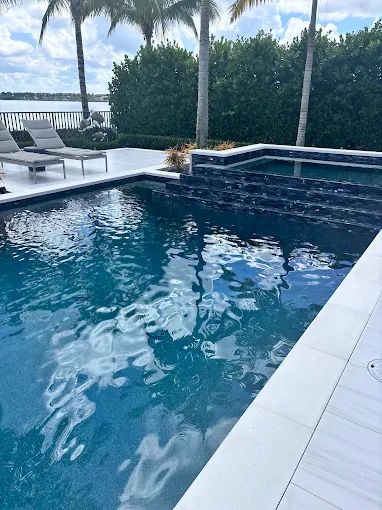 A pool deck with lounge chairs and palms behind it